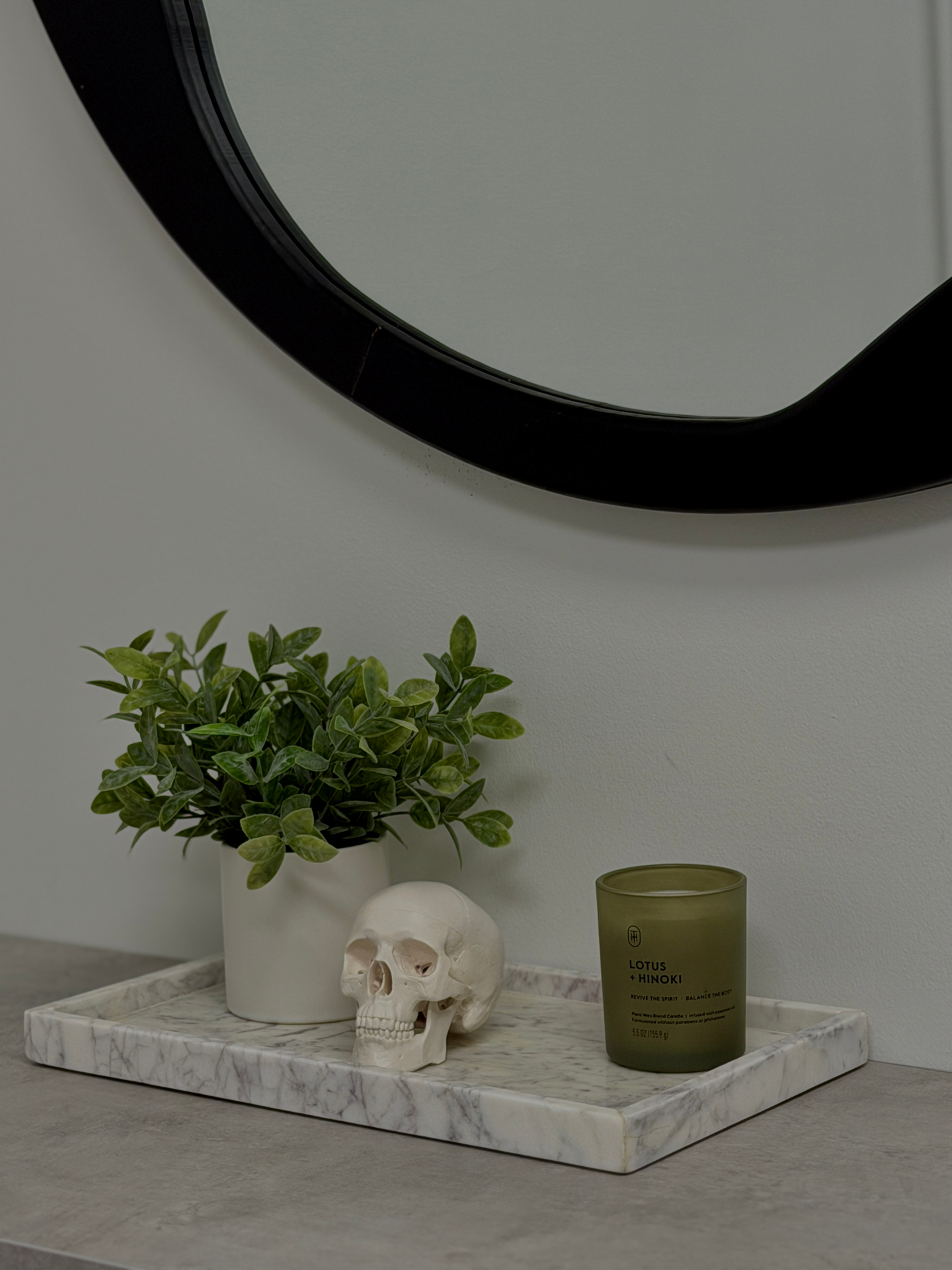 Minimalist interior detail at Lotus Aesthetics Clinic — a marble tray with a small plant, decorative skull, and lotus-scented candle beneath a round mirror