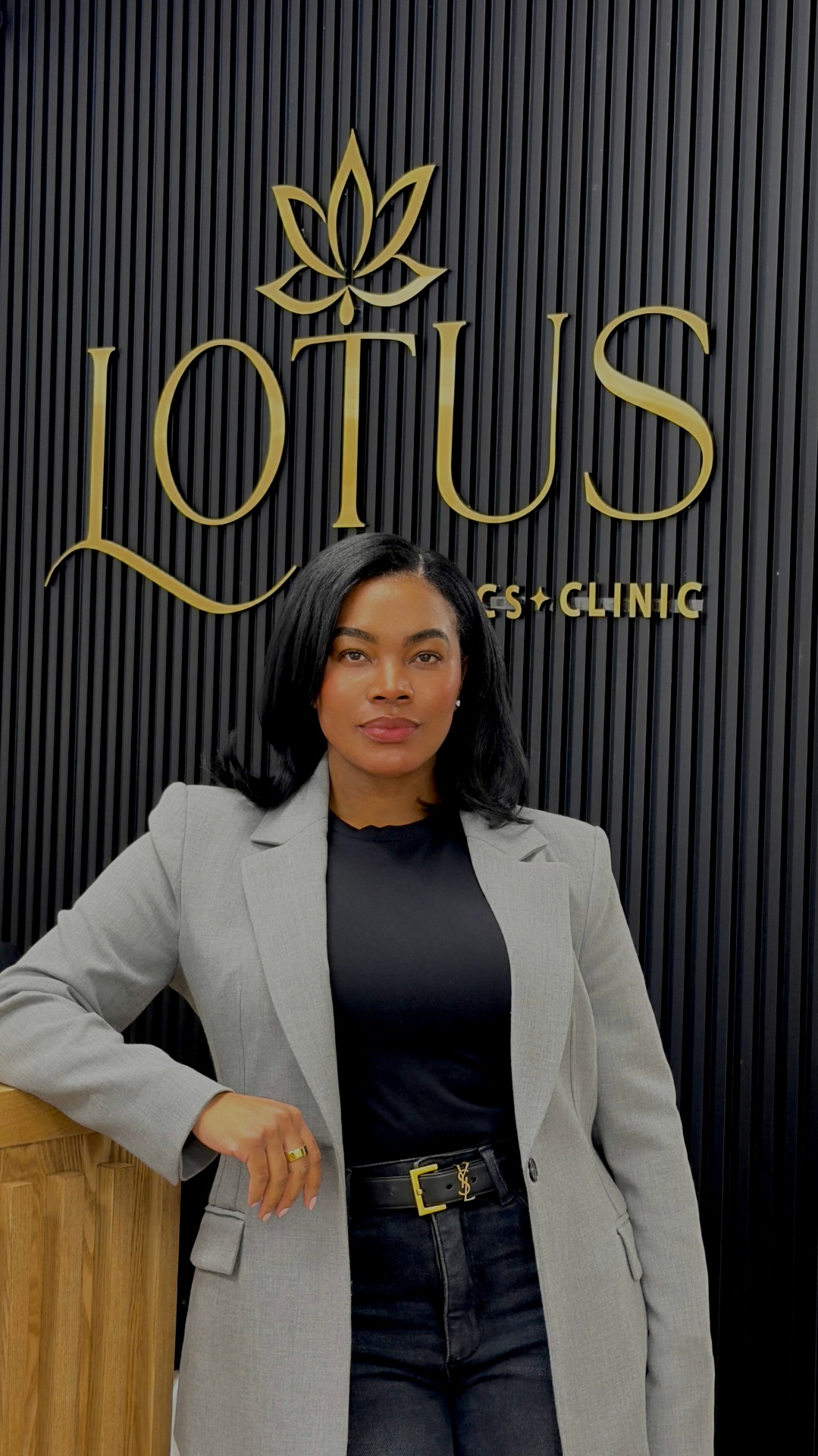 Amisha, master aesthetic nurse and injector, standing in front of the Lotus Aesthetics Clinic signage
